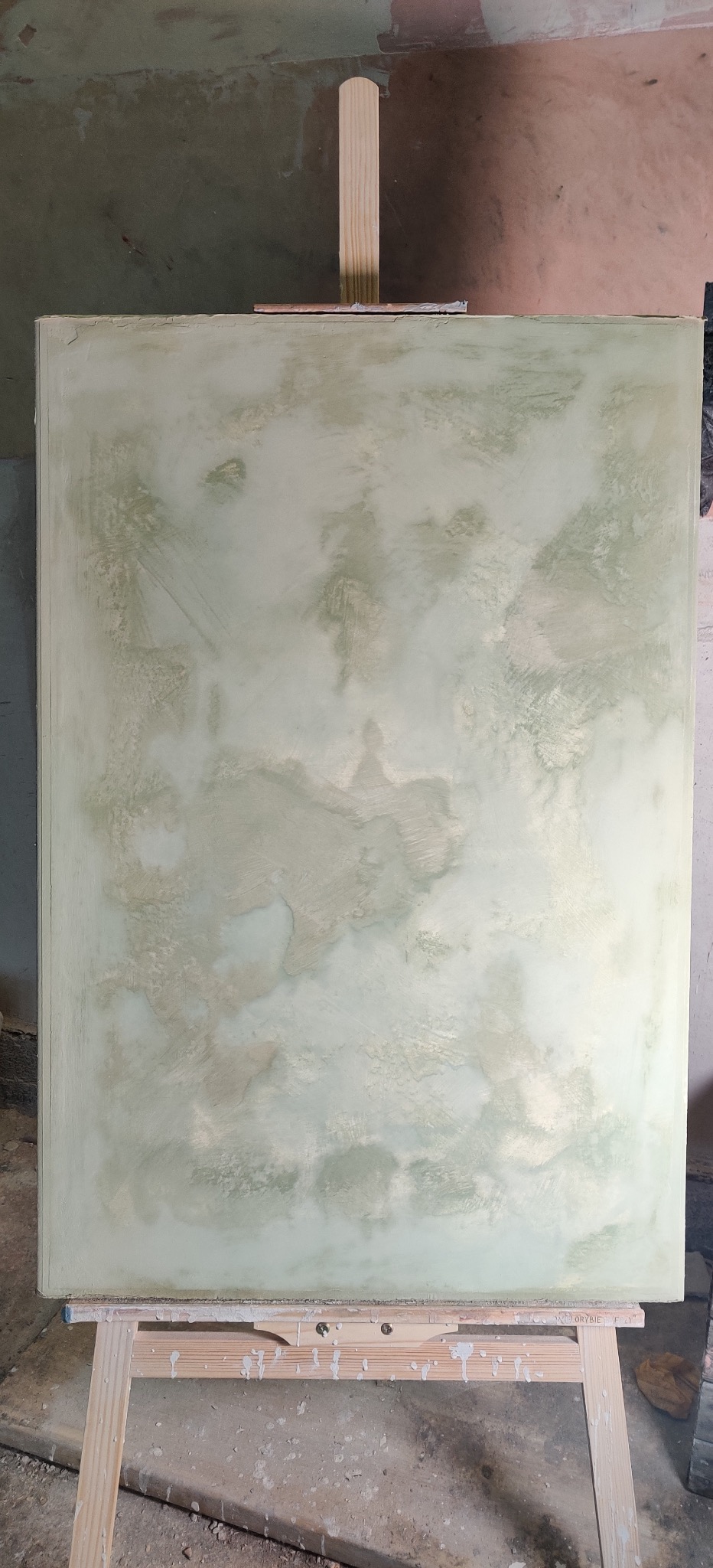 Ściana z efektem dekoracyjnym w odcieniach bieli i zieleni, umieszczona na drewnianym stojaku malarskim. Widoczne ślady farby na stojaku i podłodze.