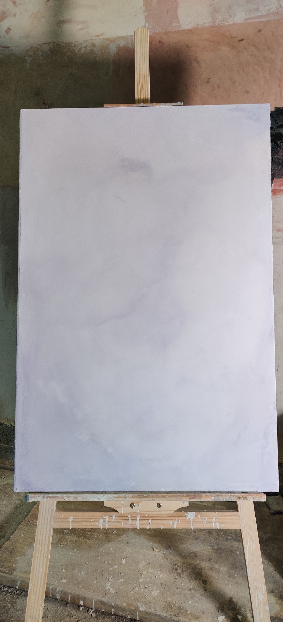 Świeżo pomalowana na biało ściana na drewnianym stojaku malarskim. Widoczne ślady farby na podłodze i stojaku. Tło ściany surowe, w odcieniach beżu i szarości.