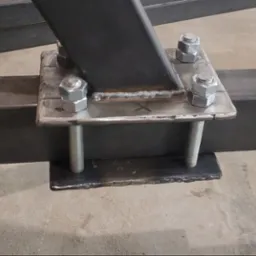 Spoina łącząca elementy konstrukcji stalowej, widoczne ślady spawania, nakrętki i śruby mocujące, surowy metal. Detal wykonania.