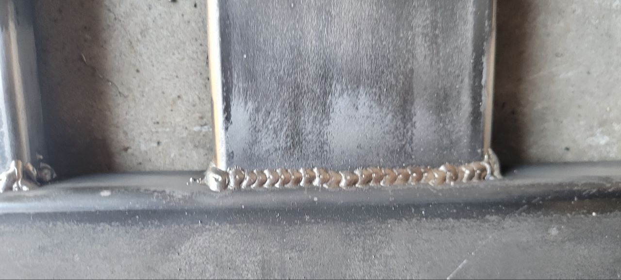 Szczegółowe zbliżenie spawu łączącego metalowe elementy konstrukcji. Widoczna faktura spoiny i szlifowana powierzchnia metalu.