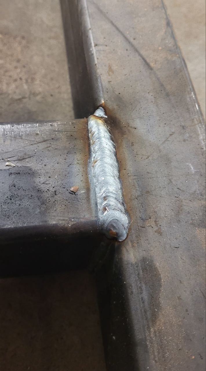 Spoina łącząca dwa metalowe profile pod kątem prostym, widoczne ślady obróbki termicznej i charakterystyczna faktura spoiny.