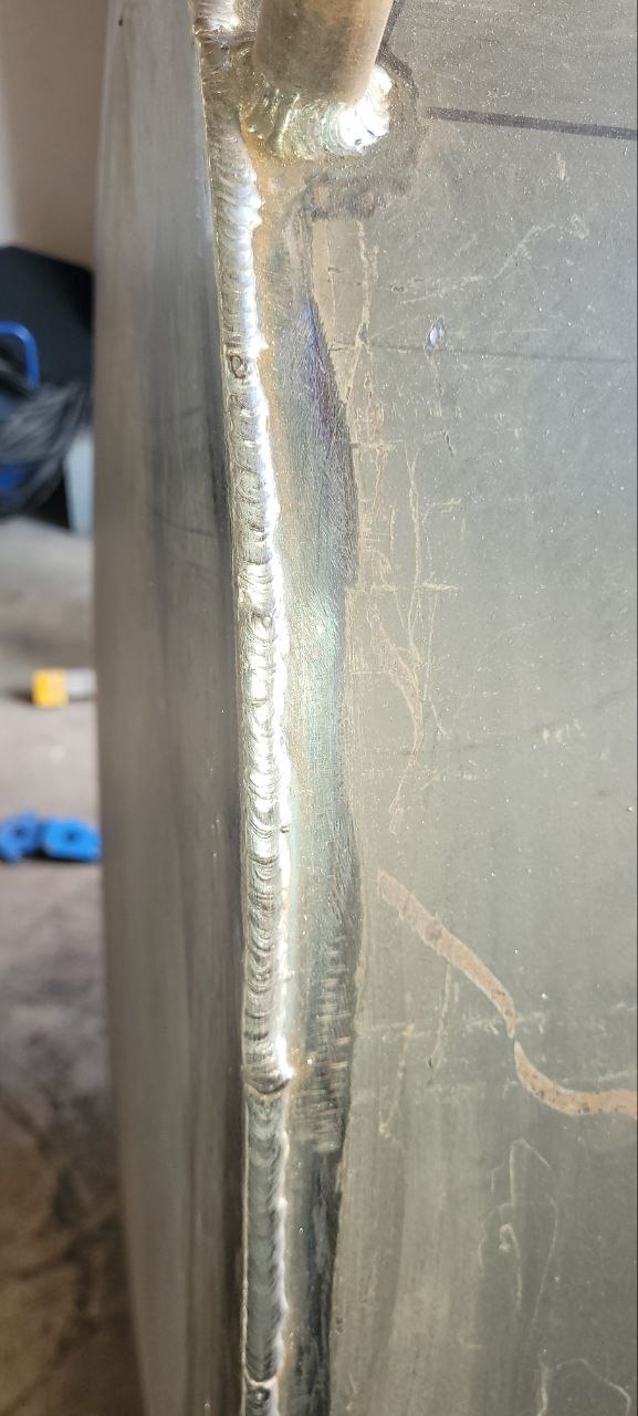 Szczegółowe zbliżenie na spawany szew łączący dwie metalowe płyty. Widoczna precyzja i estetyka wykonania spoiny. Element konstrukcji metalowej.