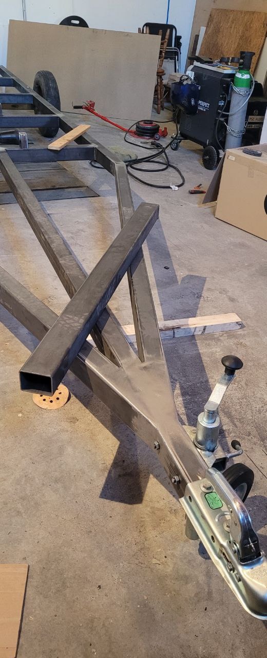 Metalowa konstrukcja przyczepy w trakcie budowy z widocznymi profilami, spawami i elementami mocującymi, na tle warsztatu z narzędziami.