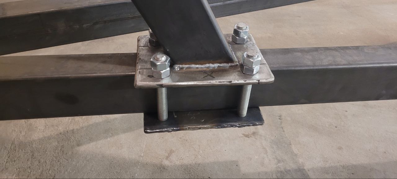 Spoina łącząca elementy konstrukcji stalowej, widoczne ślady spawania, nakrętki i śruby mocujące, surowy metal. Detal wykonania.