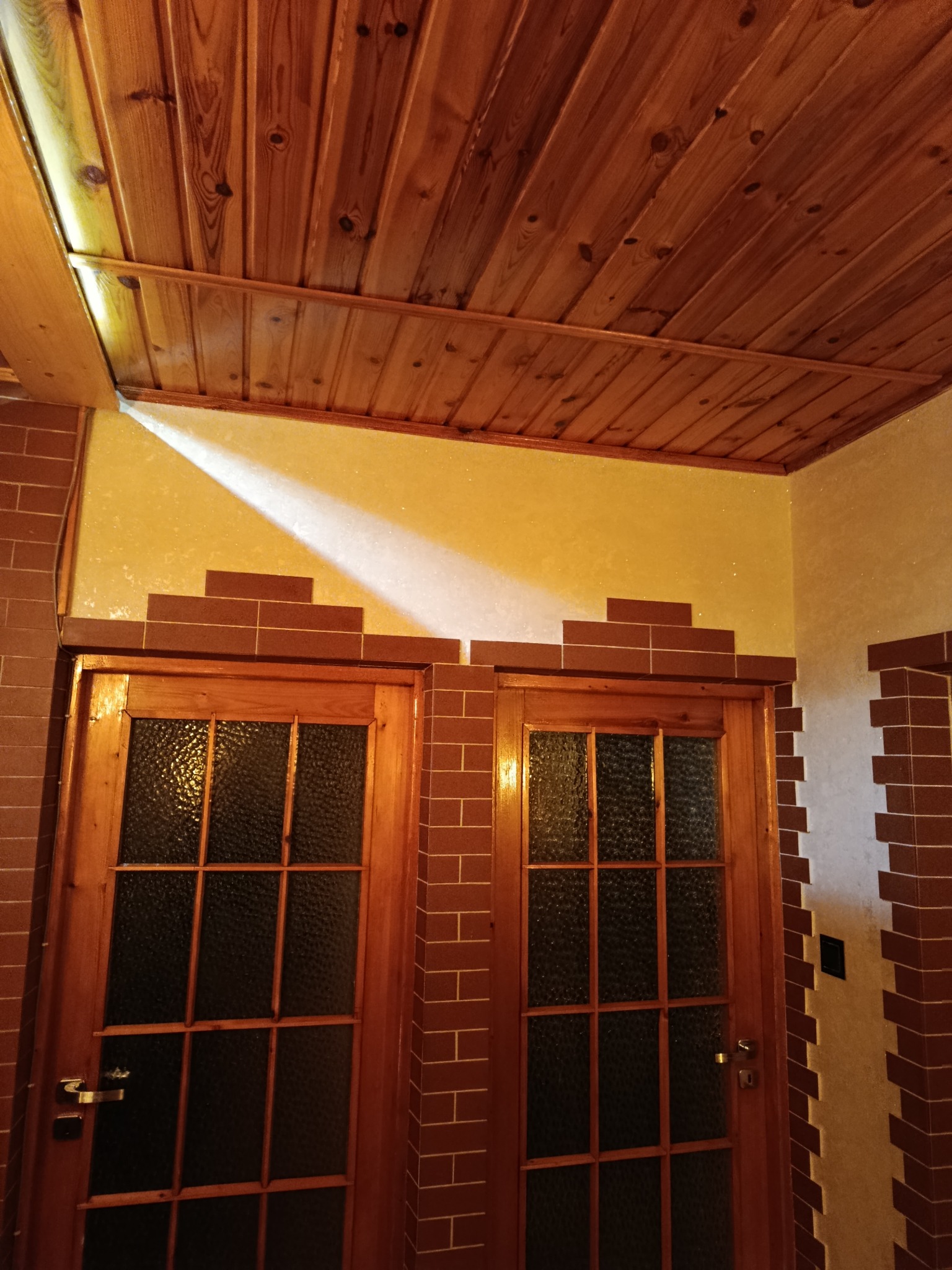 Wykończenie wnętrza z drewnianym sufitem, ścianami z cegiełek i dwuskrzydłowymi, przeszklonymi drzwiami w stylu retro. Nietypowe połączenie materiałów i faktur.