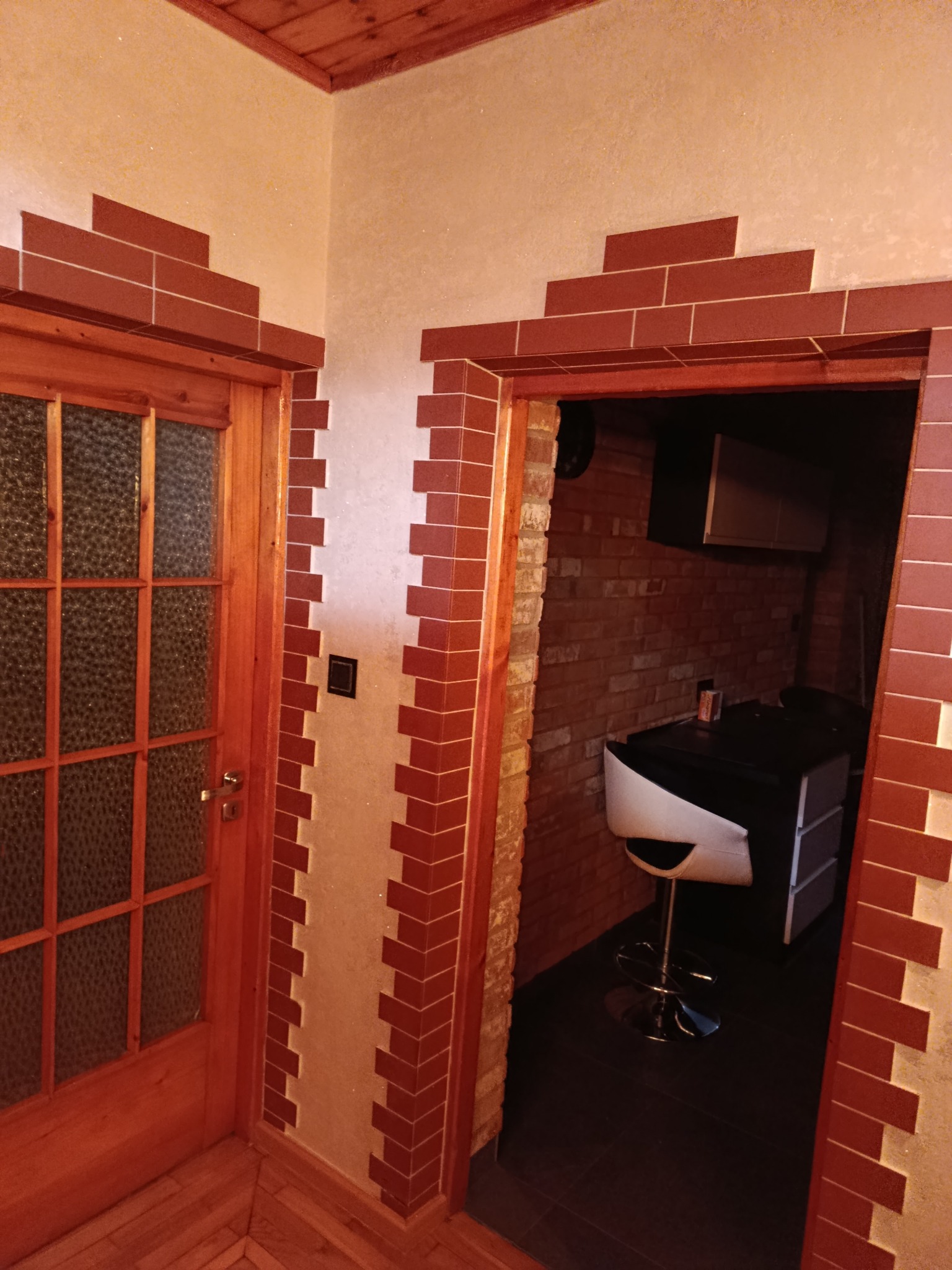 Wykończenie wnętrza z drewnianą stolarką i dekoracyjną okładziną z cegieł wokół drzwi, tworzącą unikalny wzór. Widoczny fragment podłogi z parkietu.