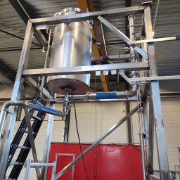 MKM WELD SERWIS - Metalowa konstrukcja wsporcza z zbiornikiem i rurami w hali produkcyjnej, widok z dołu. Widoczne spawy i elementy złączne. Na konstrukcji widnieje napis 'Eesti pagar'.