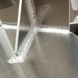 MKM WELD SERWIS - Precyzyjne spawy na konstrukcji z jasnego metalu, ukazujące detale łączeń i estetyczne wykończenie. Widoczne ślady obróbki na powierzchni metalu.