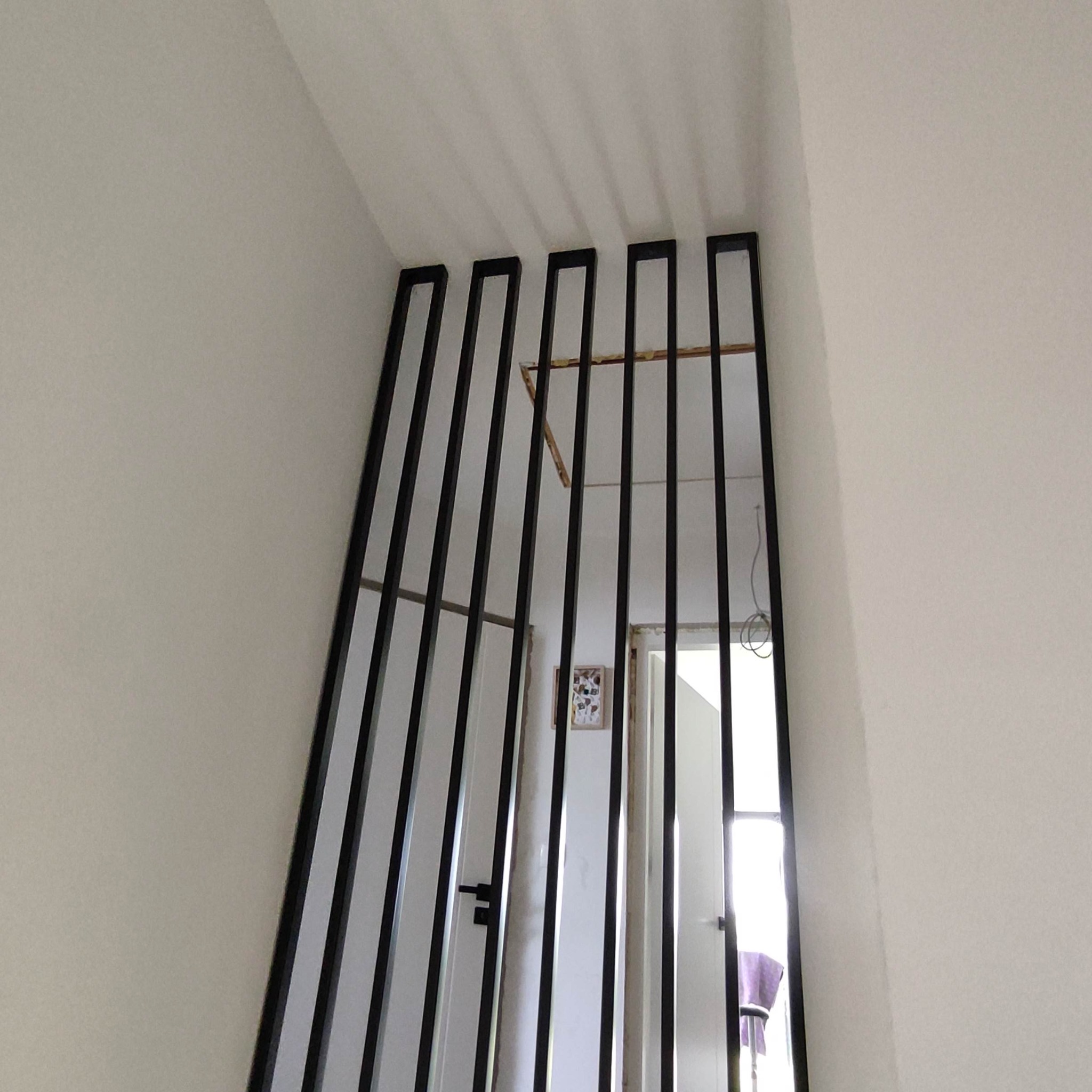 Nowoczesna, czarna balustrada schodowa z pionowych profili, widok z dołu, z fragmentem drzwi i dekoracją na ścianie w tle. Minimalistyczny design.