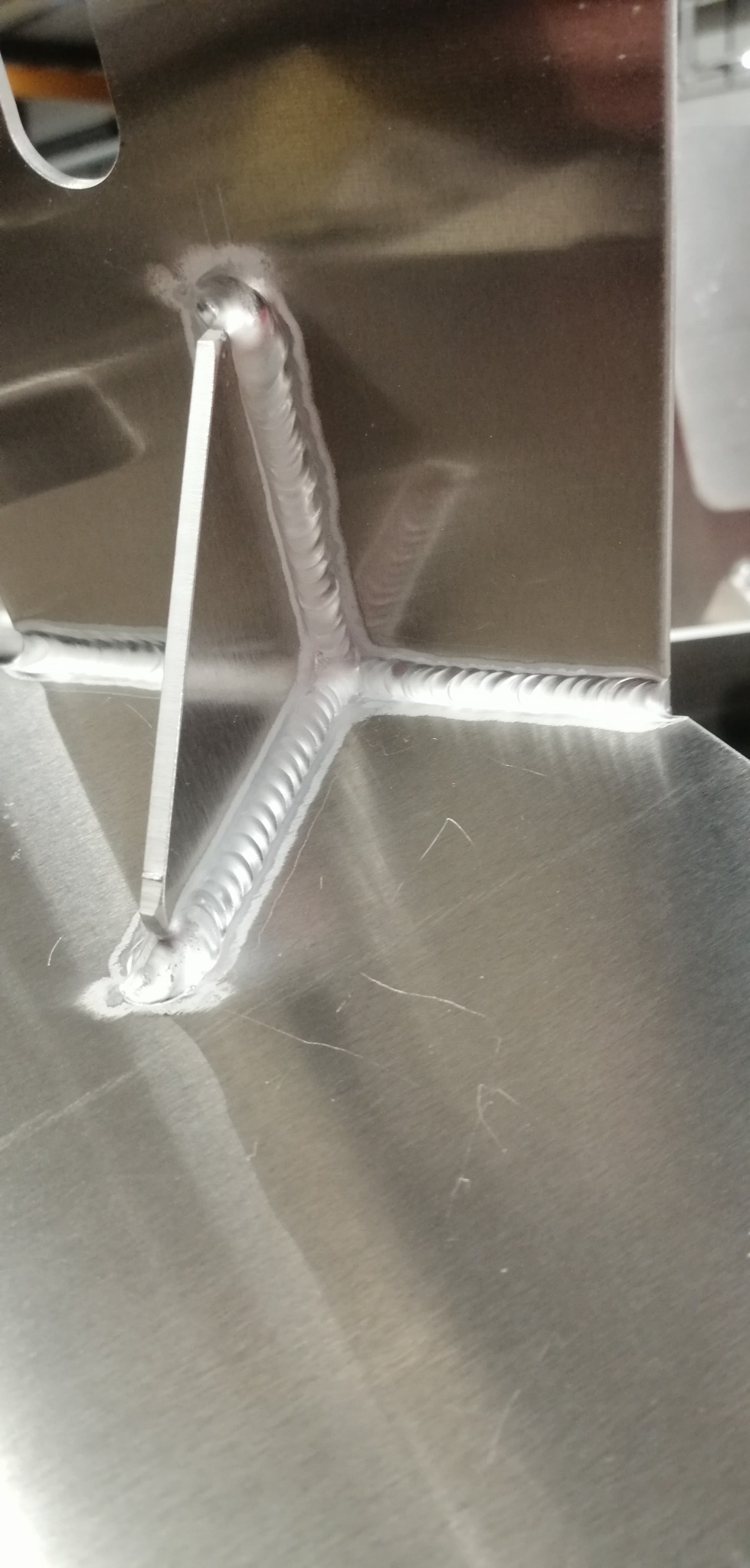 Precyzyjne spawy na konstrukcji z jasnego metalu, ukazujące detale łączeń i estetyczne wykończenie. Widoczne ślady obróbki na powierzchni metalu.