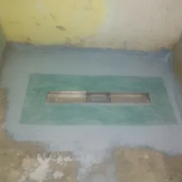 Przygotowanie podłoża pod prysznic z odpływem liniowym, zabezpieczone hydroizolacją. Widoczne ślady po pracach remontowych na ścianach i podłodze.