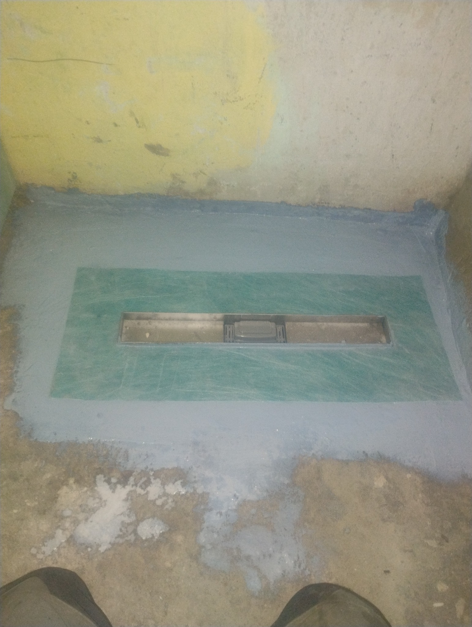 Przygotowanie podłoża pod prysznic z odpływem liniowym, zabezpieczone hydroizolacją. Widoczne ślady po pracach remontowych na ścianach i podłodze.