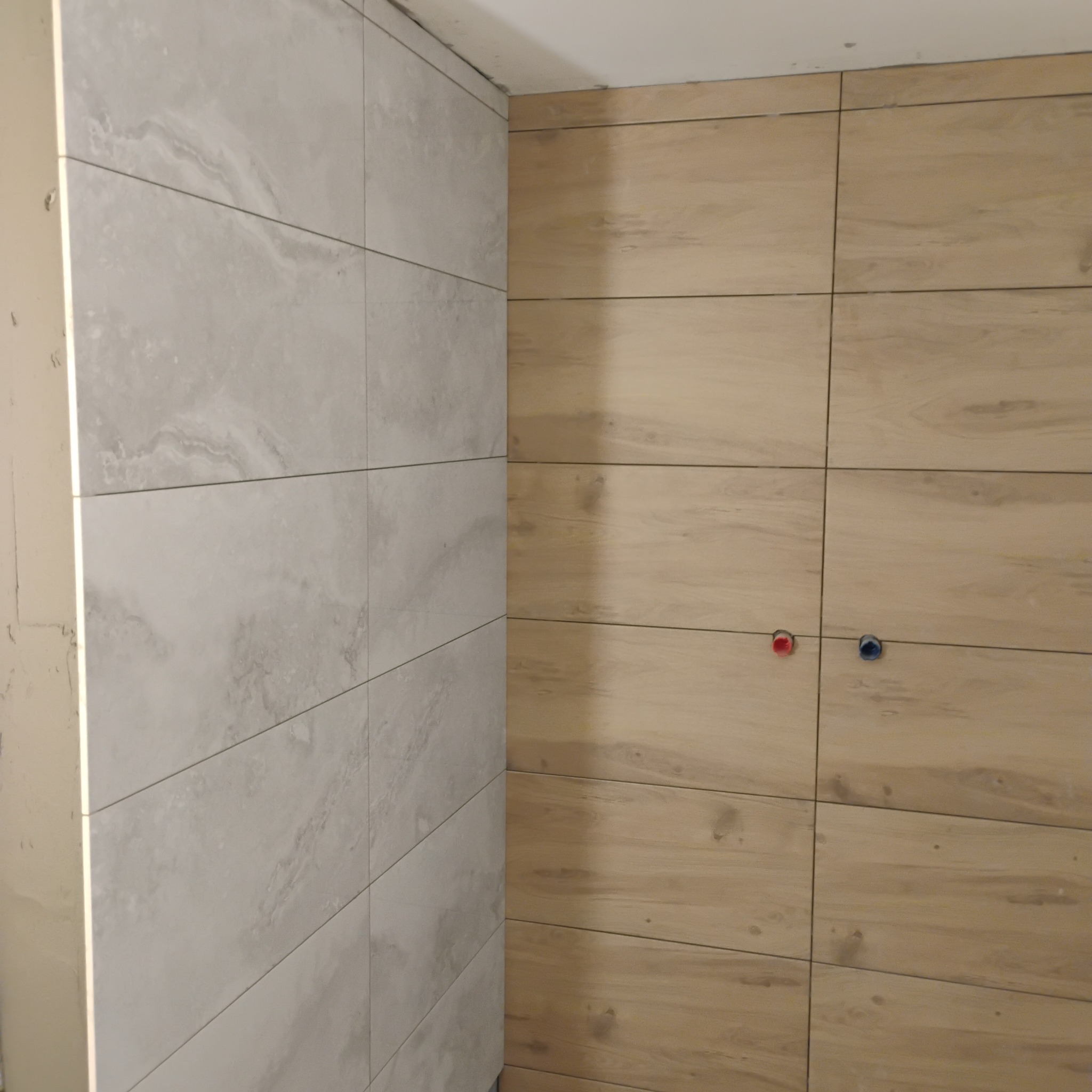 Wykończona ściana z płytek imitujących drewno i marmur, widoczne podejścia wodne. Jasne kolory, minimalistyczny design.