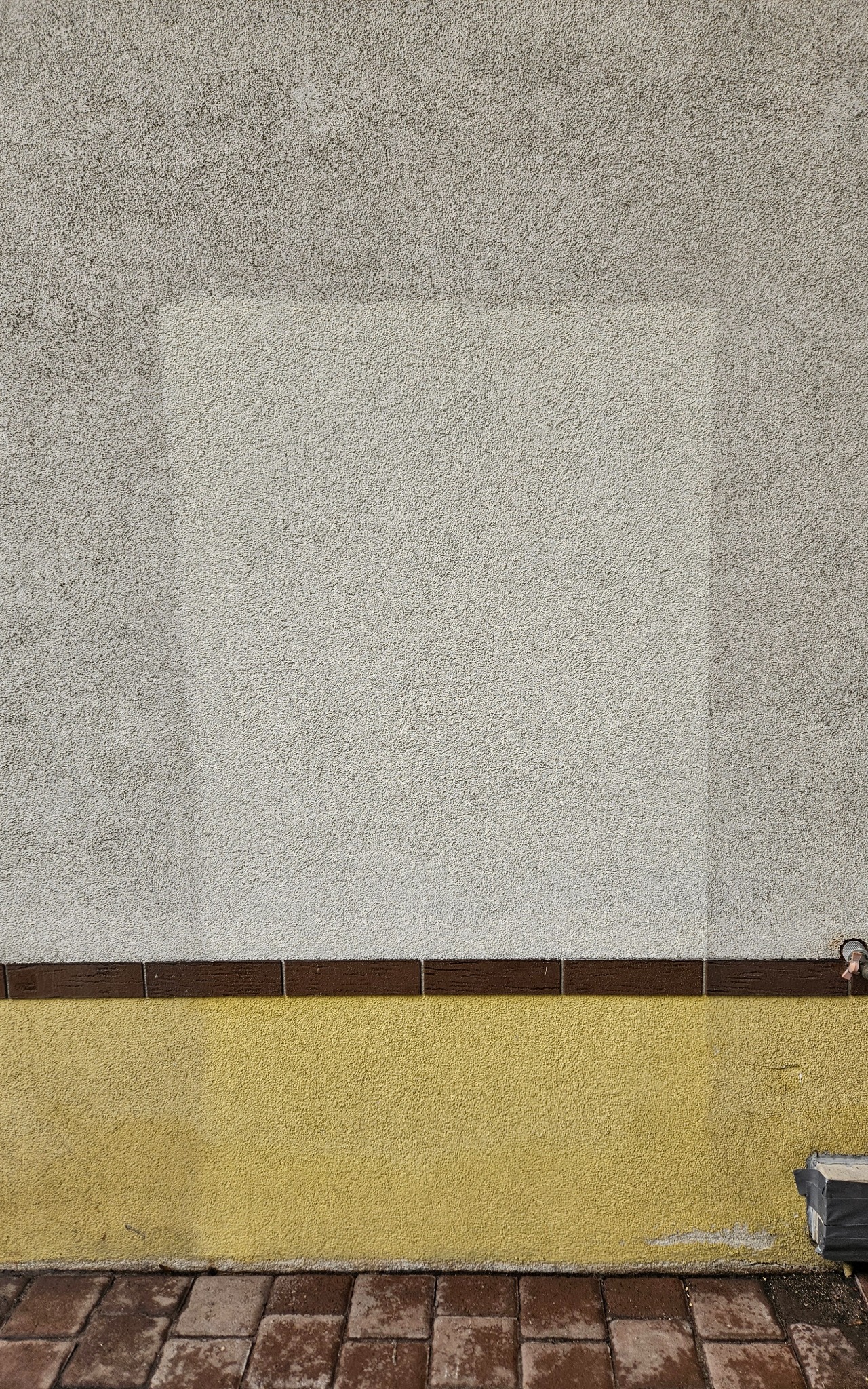Fragment elewacji budynku z widocznym obszarem po czyszczeniu, kontrastującym z zabrudzoną powierzchnią. Żółty cokół i brązowe płytki dodają koloru.