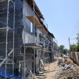 Dom w trakcie ocieplania: czarny styropian na elewacji, rusztowania, worki z zaprawą. Widok z boku na budynek w trakcie prac izolacyjnych.