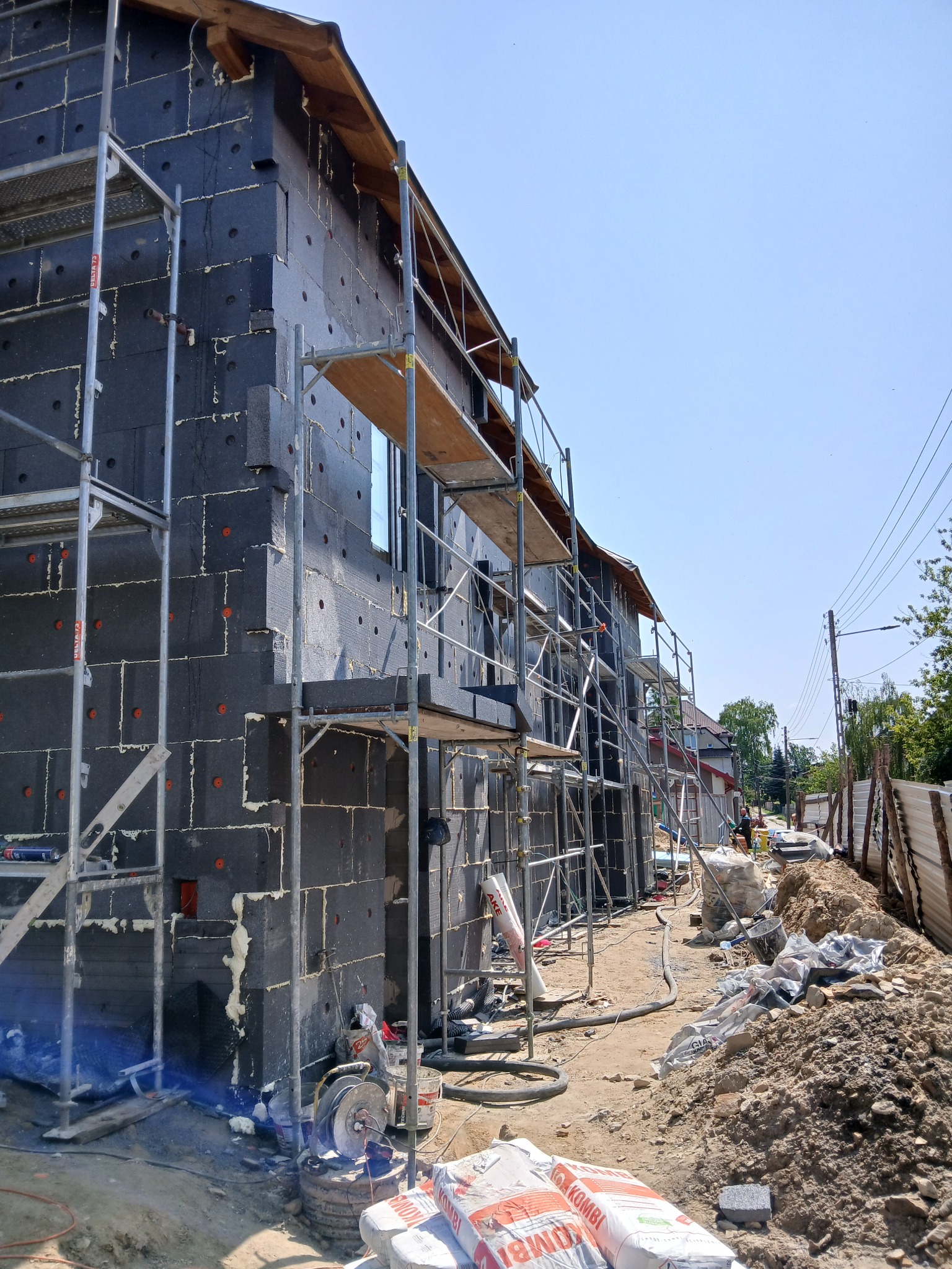 Dom w trakcie ocieplania: czarny styropian na elewacji, rusztowania, worki z zaprawą. Widok z boku na budynek w trakcie prac izolacyjnych.