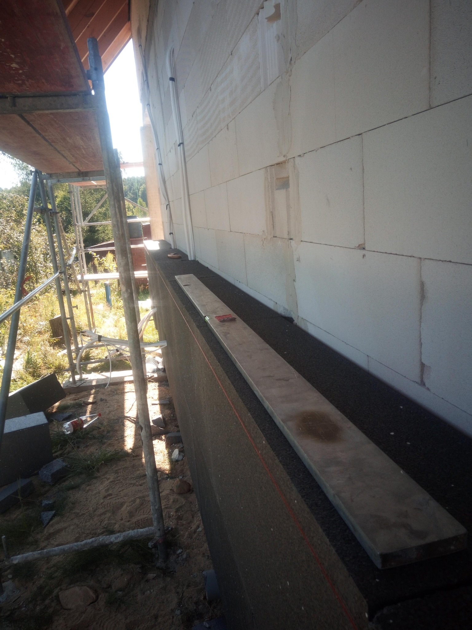 Ocieplanie ściany budynku z bloczków, widoczne płyty izolacyjne i rusztowanie. Etap prac z przygotowaniem do dalszego ocieplenia. Widok z dołu, z boku.