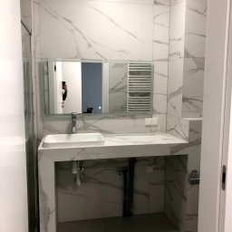 Rivano - Nowoczesna łazienka z marmurowymi płytkami, prostokątną umywalką i grzejnikiem drabinkowym. W lustrze odbija się osoba robiąca zdjęcie.