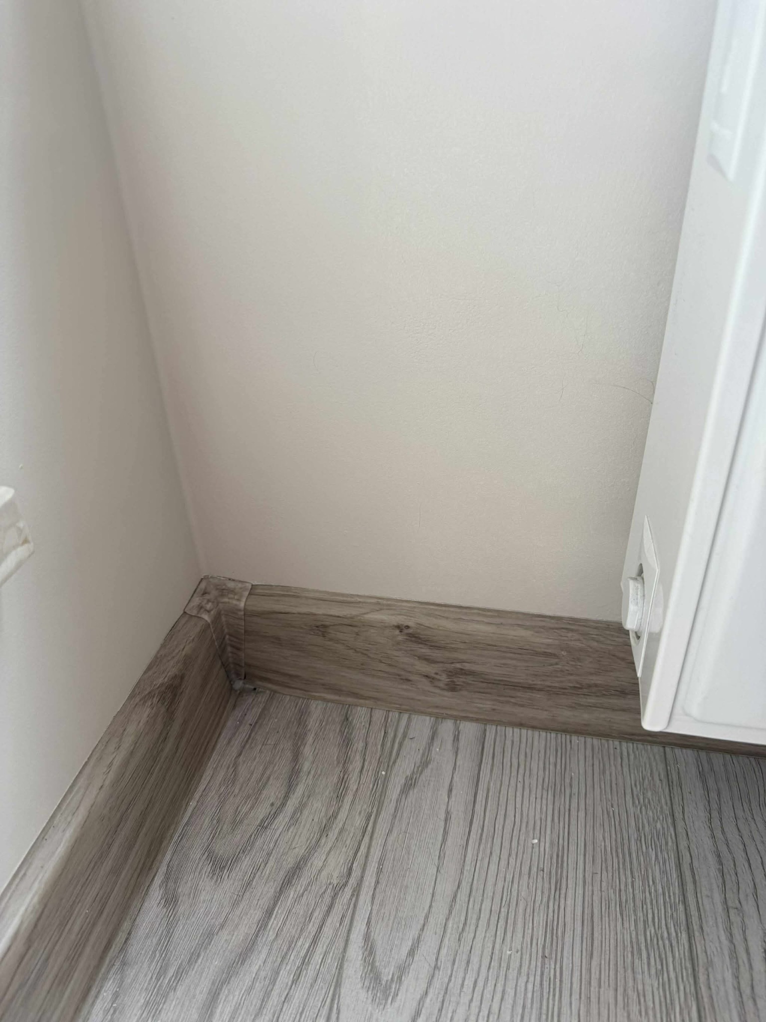 Szczegółowe ujęcie świeżo pomalowanej ściany w odcieniach bieli, z nową przypodłogową listwą w kolorze drewna i fragmentem grzejnika.