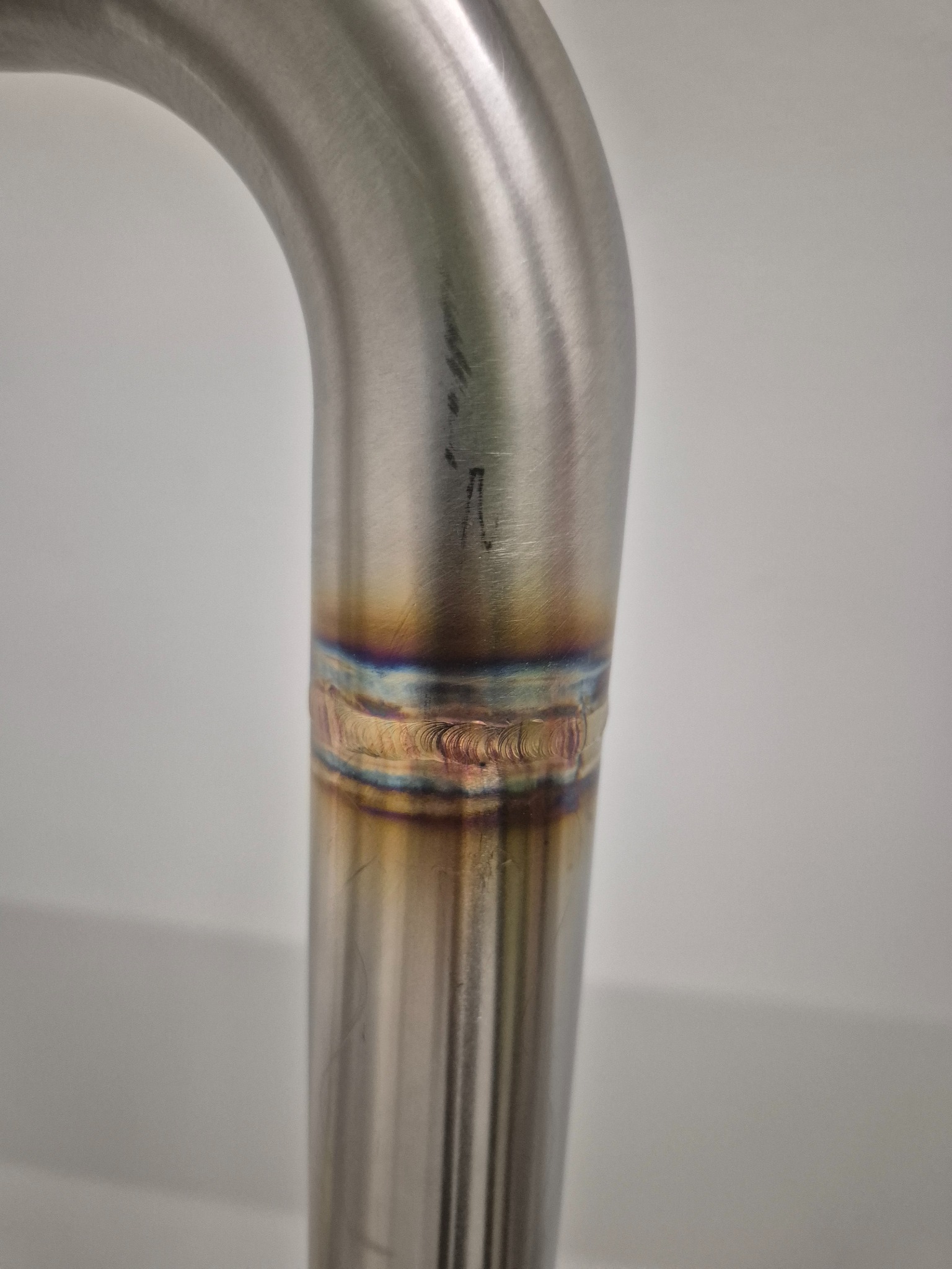 Szczegółowe zbliżenie na spawany element z metalu, ukazujący precyzyjne łączenie z widocznymi kolorami spoiny. Widoczne ślady po obróbce.