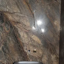 Wykończona ściana łazienki z marmuru Rainforest Brown, widoczne elementy instalacji wodnej i odpływu. Dekoracyjny kamień z wyraźnym rysunkiem żył.