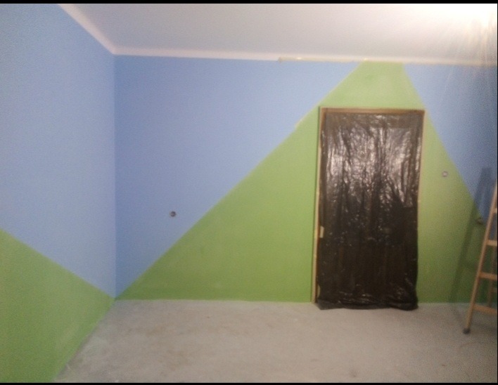 Pokój po malowaniu ścian w geometryczne wzory (błękit i zieleń), zabezpieczone drzwi folią malarską, drabina oparta o ścianę. Nietypowe połączenie kolorów.