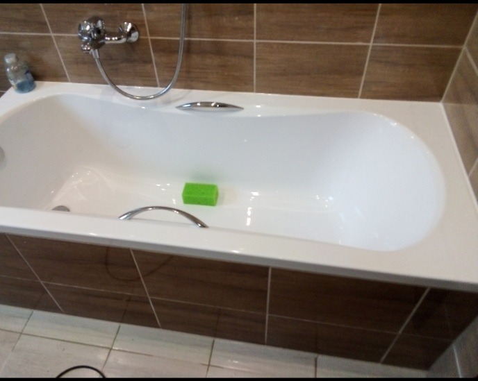 Biała wanna z brązowymi płytkami, chromowaną armaturą i zieloną gąbką. Widoczne detale wykończenia i czystość powierzchni.