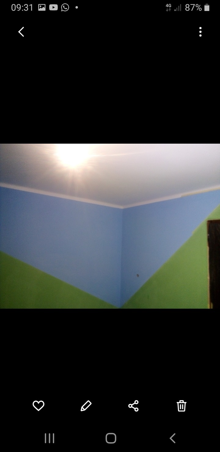 Pomysłowe malowanie ścian w pokoju: górna część na niebiesko, dolna na zielono, oddzielone ukośną linią. Biały sufit z widocznym oświetleniem.