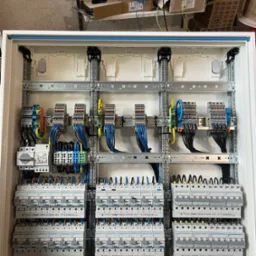Rozdzielnica elektryczna Hager z licznymi zabezpieczeniami, widoczne przewody i złączki. Precyzyjny montaż w białej obudowie. Szare szyny montażowe.