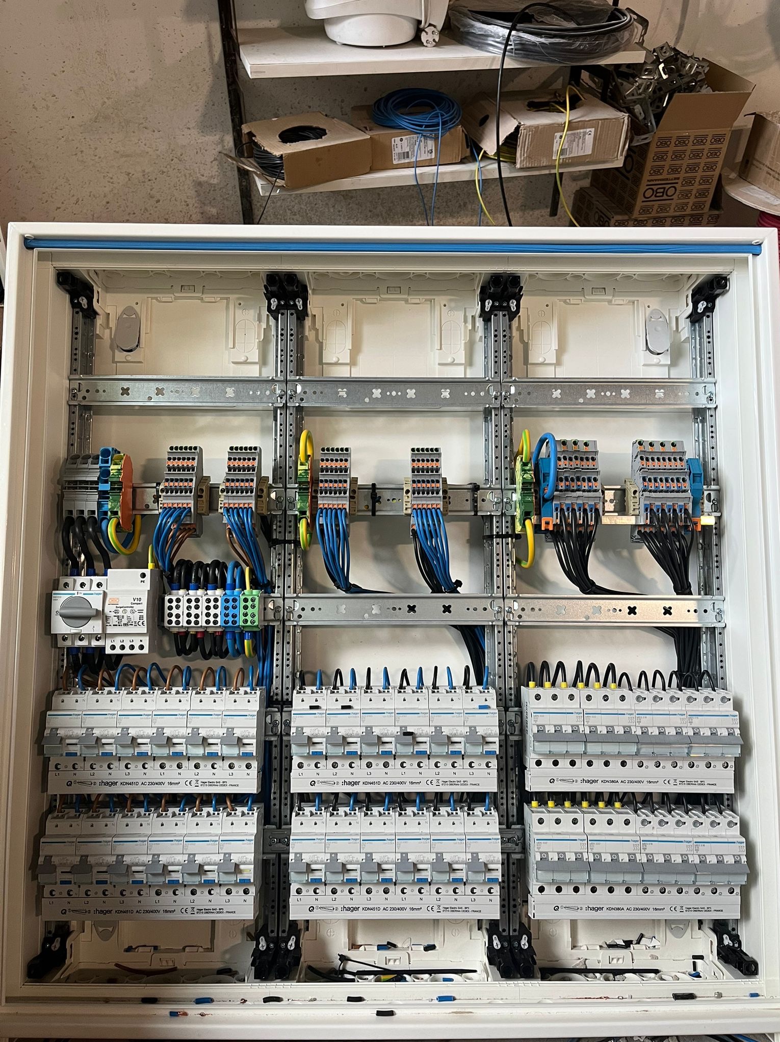 Rozdzielnica elektryczna Hager z licznymi zabezpieczeniami, widoczne przewody i złączki. Precyzyjny montaż w białej obudowie. Szare szyny montażowe.