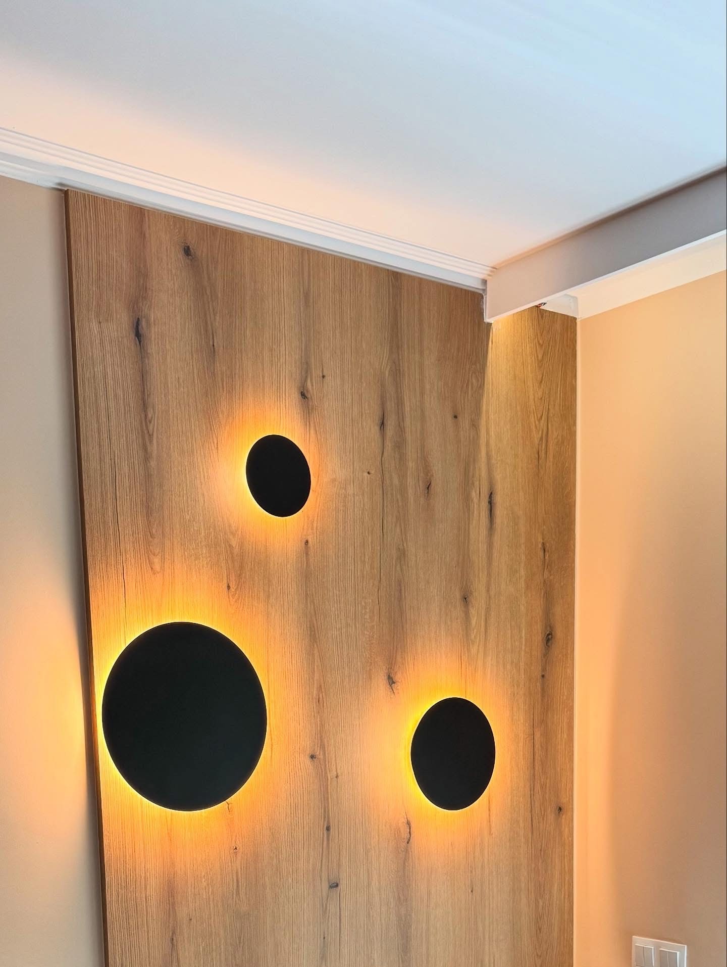 Drewniana ściana z trzema okrągłymi, podświetlanymi elementami dekoracyjnymi, tworzącymi unikalny efekt świetlny w nowoczesnym wnętrzu.