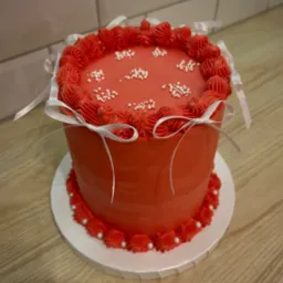 Czerwony tort z kremem i białymi perełkami, ozdobiony wstążkami, na drewnianym blacie i tle z białych płytek. Dekoracja tortu w stylu minimalistycznym.