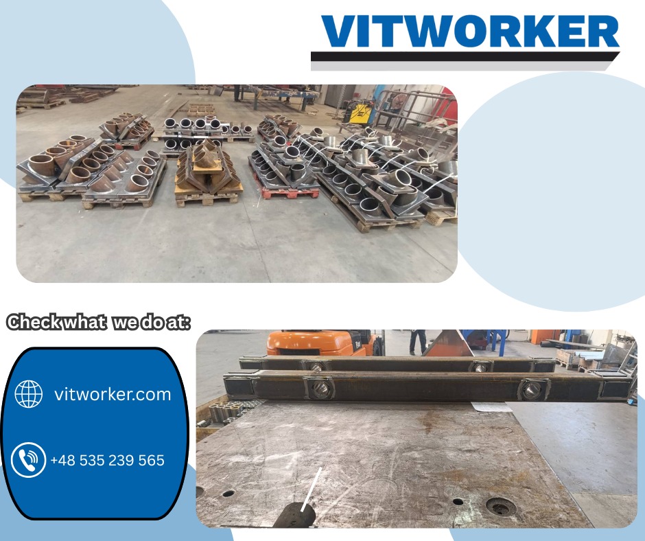 Metalowe elementy konstrukcyjne na paletach i stole warsztatowym. Widoczne spawy i otwory. Elementy przygotowane do dalszej obróbki lub montażu. Hala produkcyjna w tle.