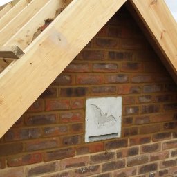 OPTIROOMS SERVICE & CONSTRUCTION SPÓŁKA Z OGRANICZONĄ ODPOWIEDZIALNOŚCIĄ - Wznoszenie muru z cegły z otworem wentylacyjnym dla nietoperzy, widoczne drewniane elementy konstrukcji dachu. Ujęcie z budowy domu w trakcie prac murarskich.