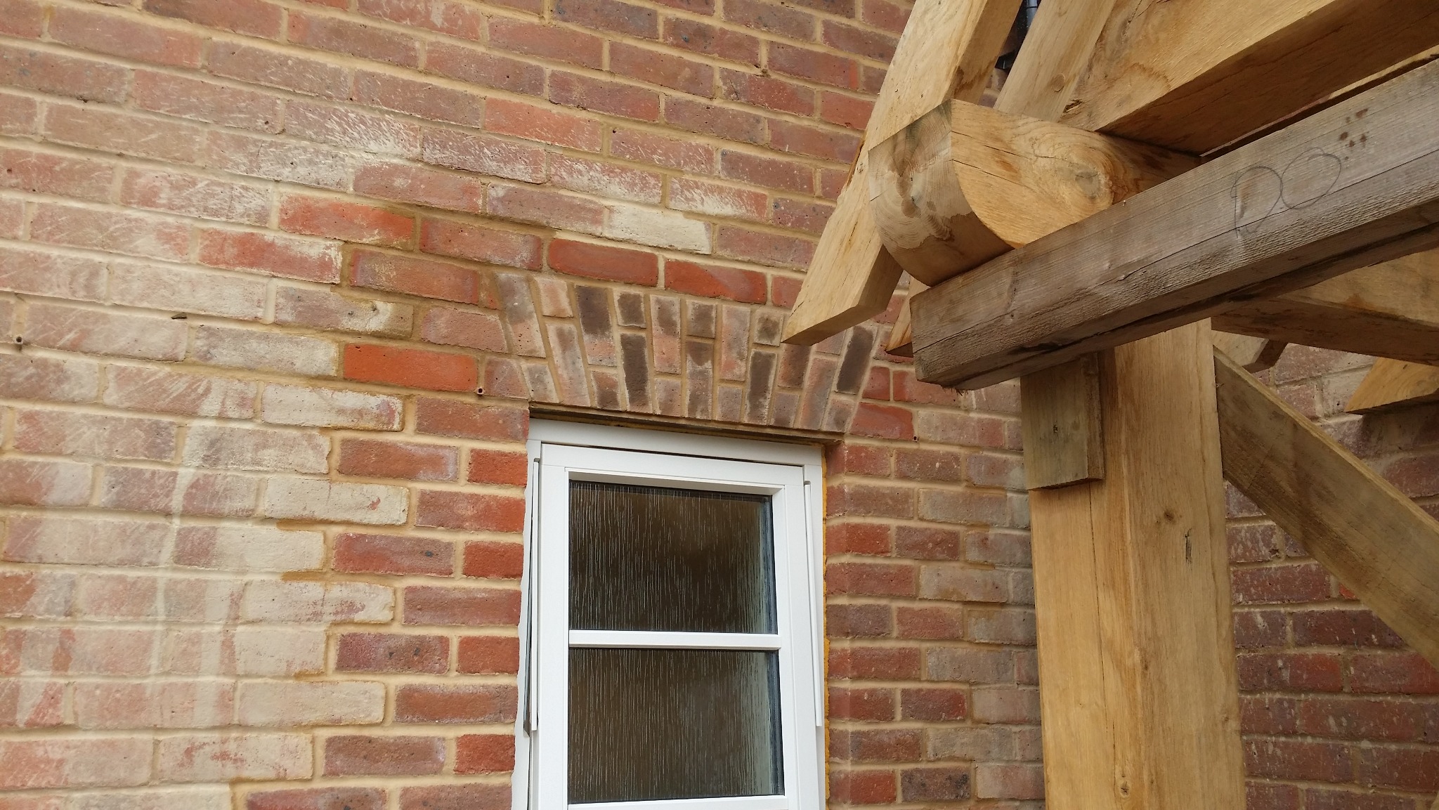 Murowana ściana z cegły z oknem i drewnianą konstrukcją. Widoczny łuk nad oknem z cegły, drewniane elementy konstrukcyjne. Detal budowlany.