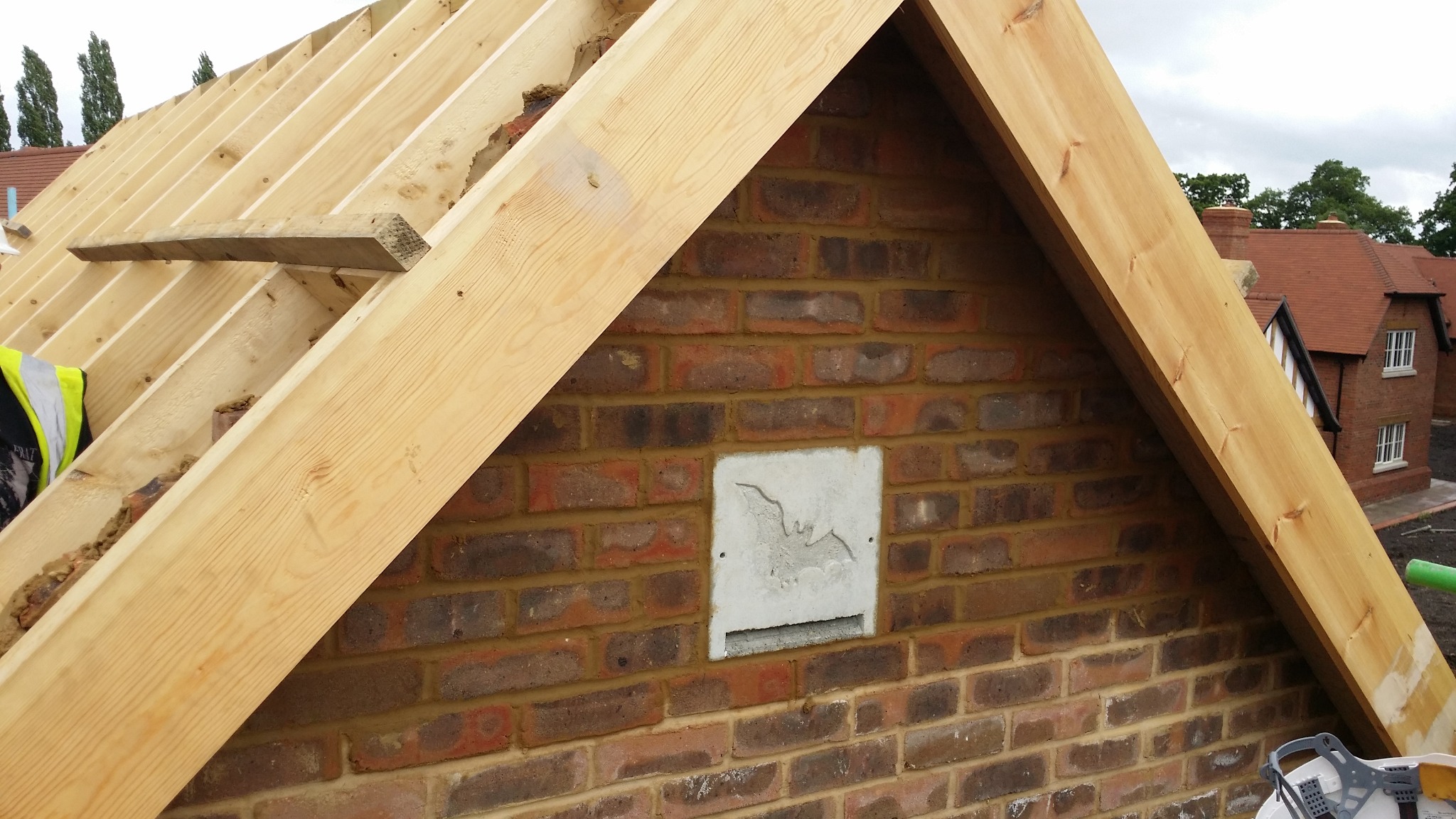 Wznoszenie muru z cegły z otworem wentylacyjnym dla nietoperzy, widoczne drewniane elementy konstrukcji dachu. Ujęcie z budowy domu w trakcie prac murarskich.
