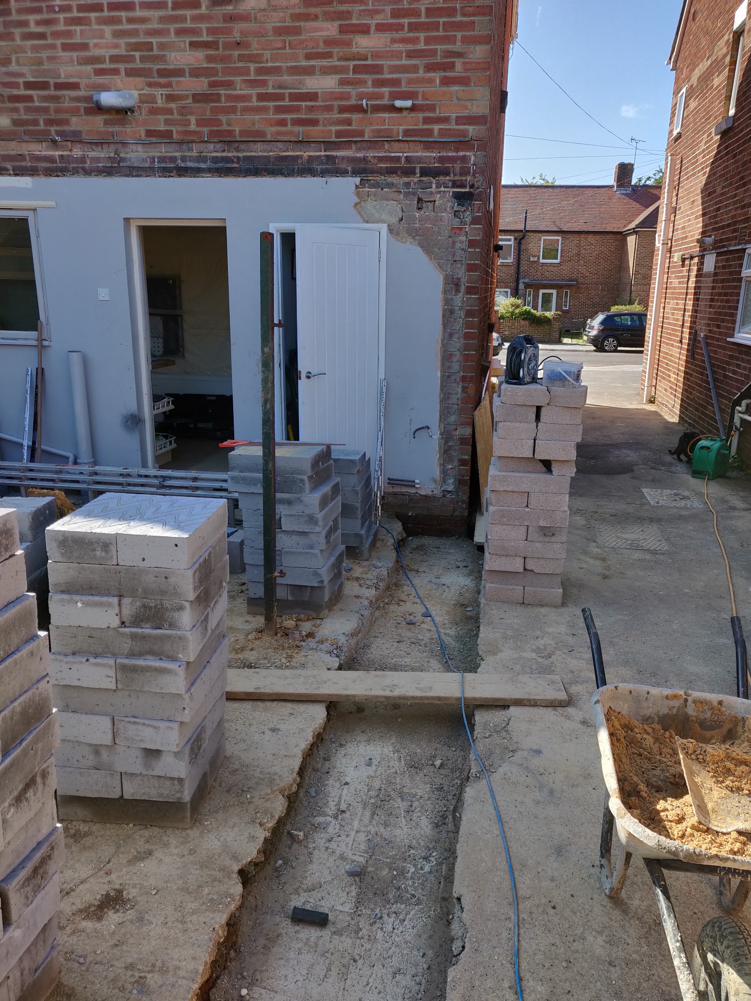 Przygotowanie do murowania ścian: wykopany fundament, ułożone bloczki, taczka z zaprawą. Widoczny fragment budynku w trakcie prac murarskich.