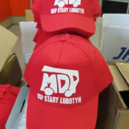 Czerwone czapki z białym nadrukiem 'MDP OSP Stary Lubotyń' ułożone jedna na drugiej. Widoczne detale nadruku i faktura materiału czapek.