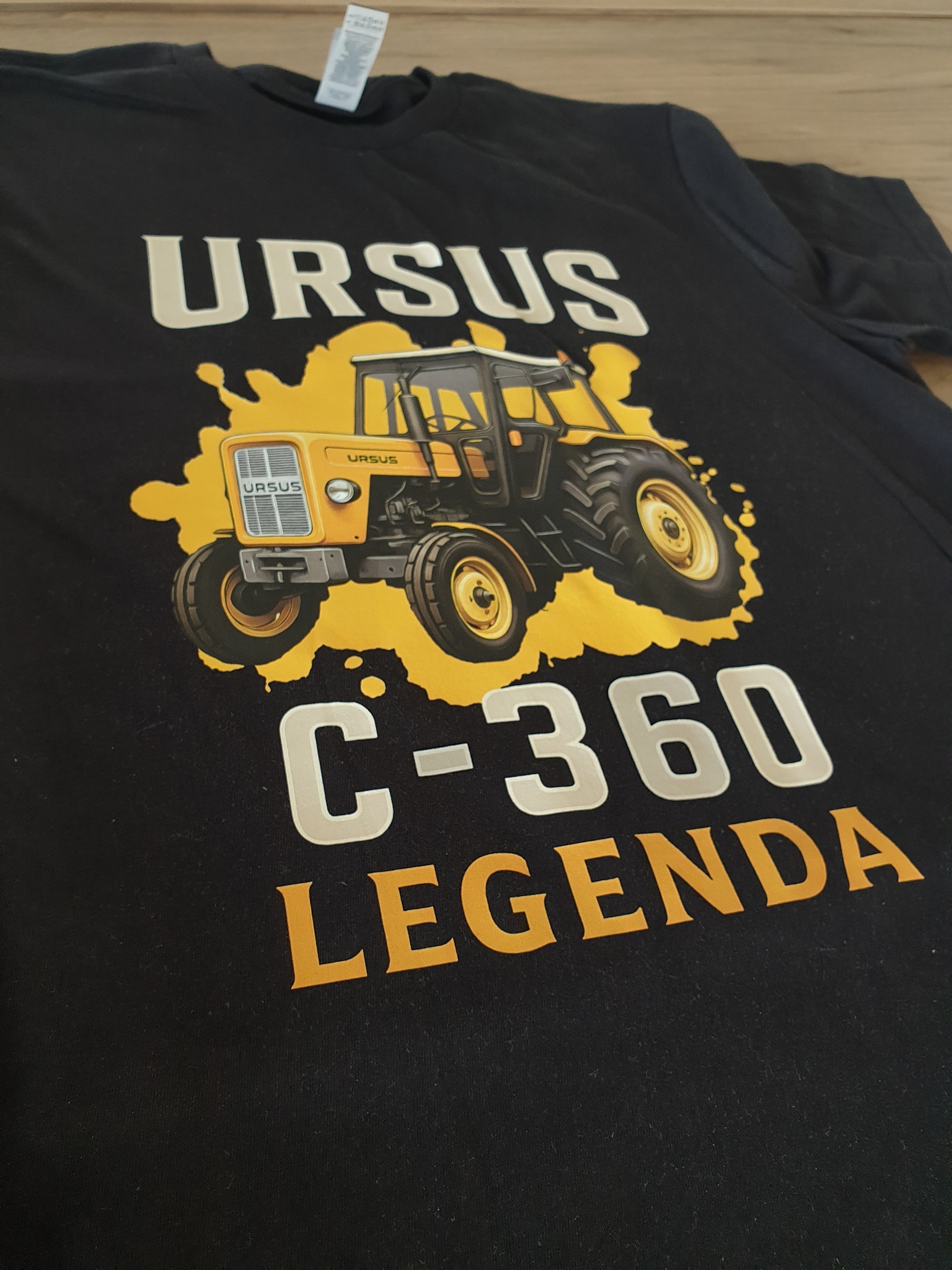 Czarna koszulka z nadrukiem żółtego traktora Ursus C-360 i napisem 'Legenda'. Grafika w stylu vintage, lekko zniekształcona perspektywa, widoczny fragment metki.