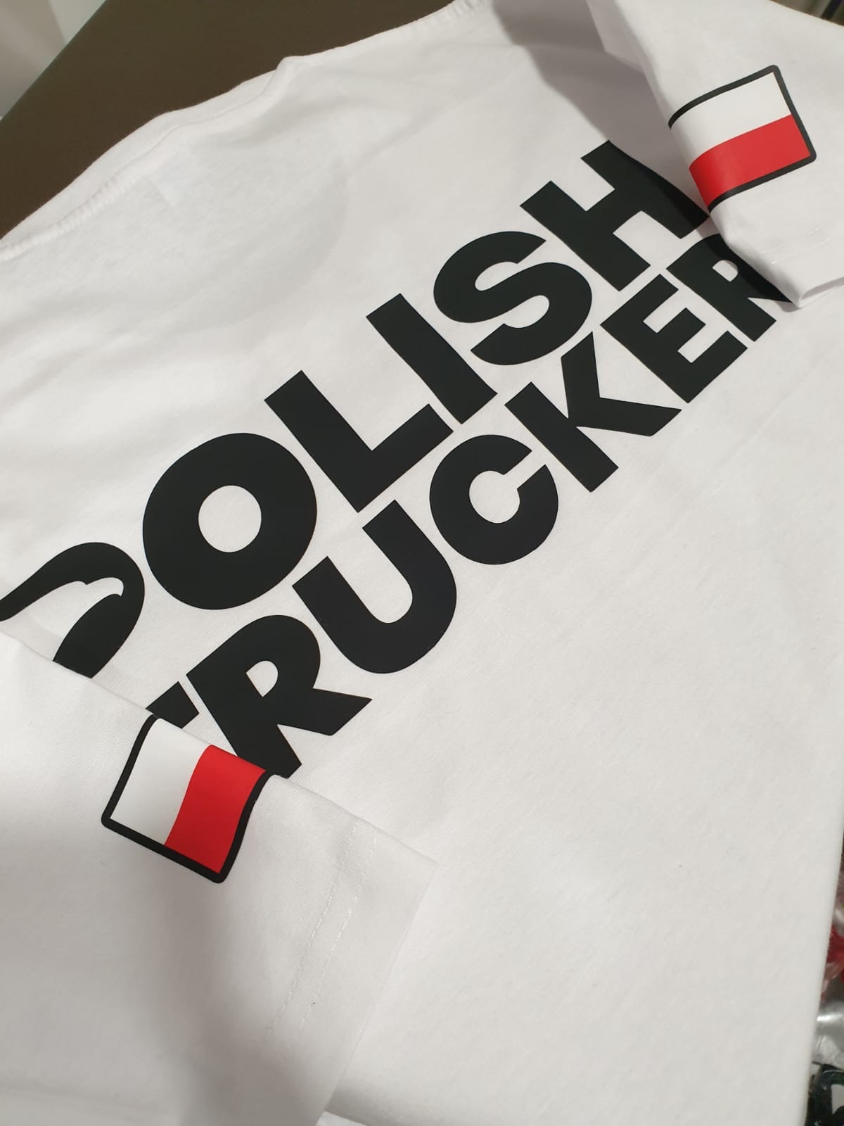 Biała koszulka z czarnym nadrukiem 'POLISH TRUCKER' i flagą Polski na rękawie, wykonana w Świebodzicach. Widok z bliska.