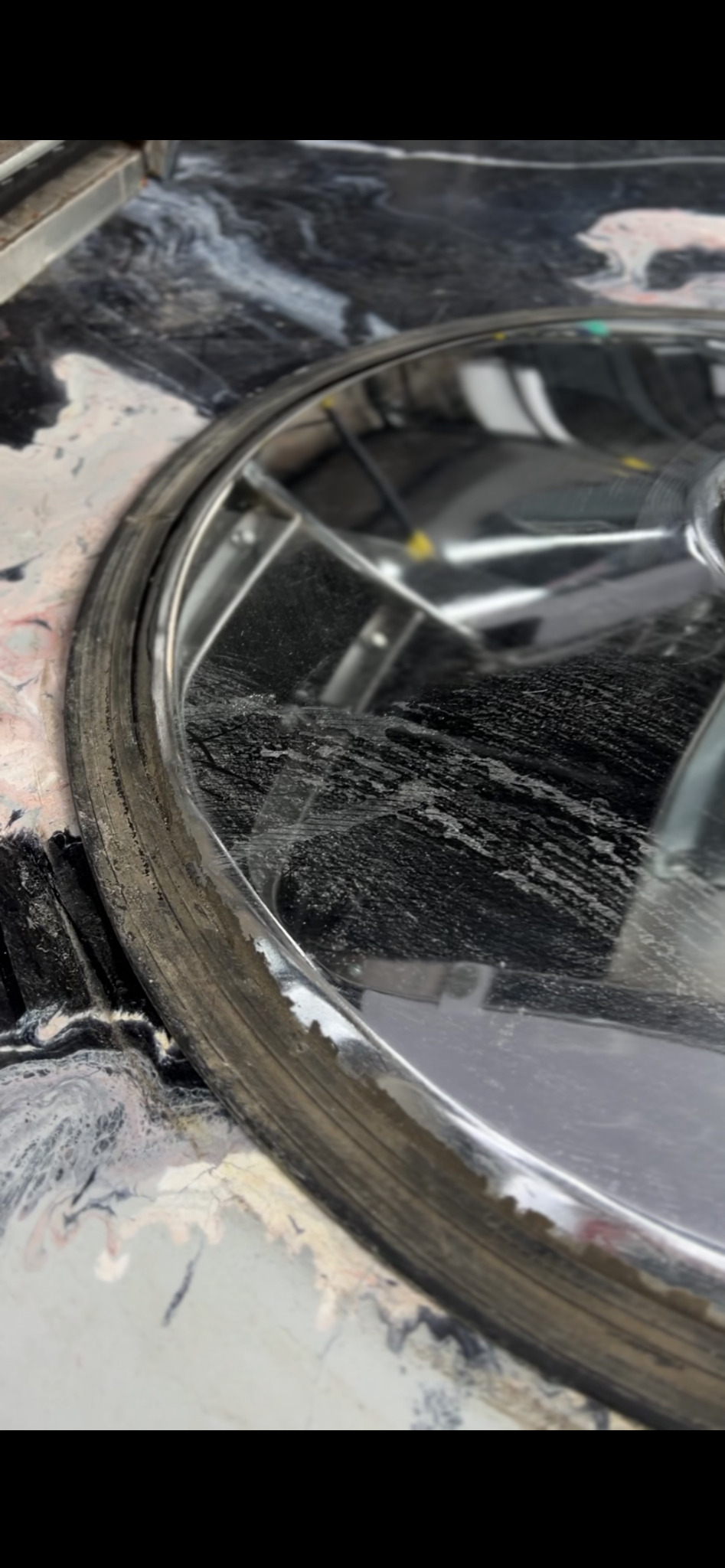 Zlew z czarnego marmuru z osadami i zaciekami, widoczne ślady po czyszczeniu. Metalowy rant zlewu z widocznymi zabrudzeniami. Ujęcie z bliska, z góry.