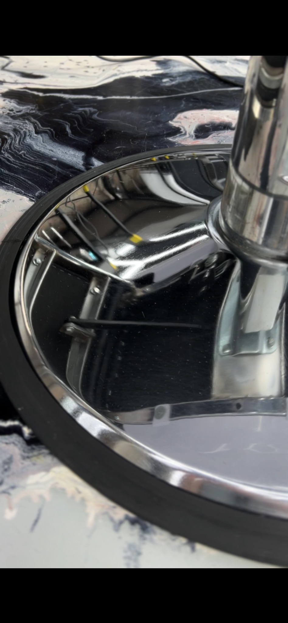 Błyszcząca, chromowana podstawa krzesła fryzjerskiego na marmurowym blacie. Widoczne ślady po czyszczeniu, brak smug. Detaliczny widok na czystą powierzchnię.