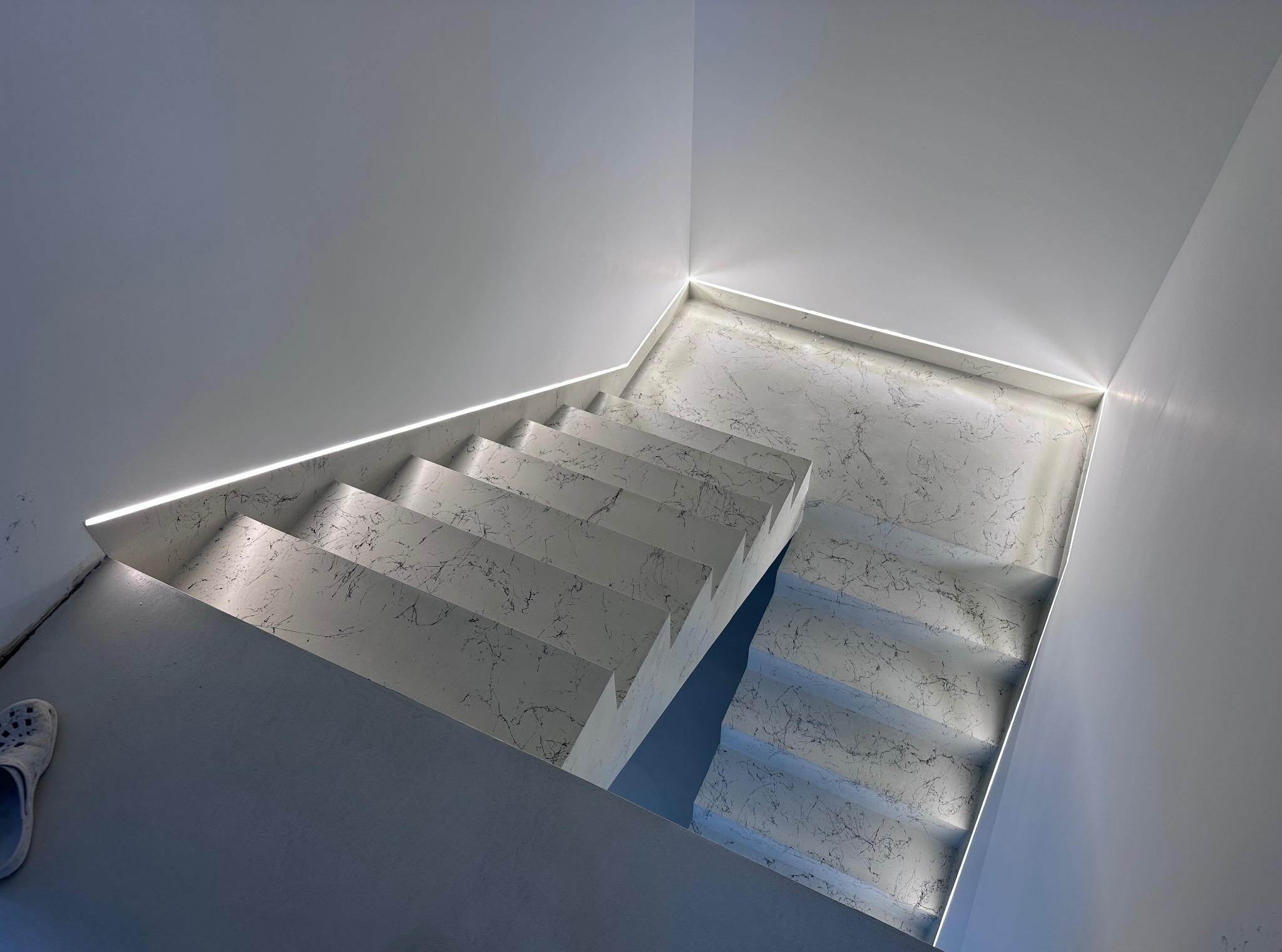 Nowoczesne schody z marmurowym wzorem, podświetlone subtelnym światłem LED, tworzące minimalistyczny i elegancki design wnętrza. Widok z góry.