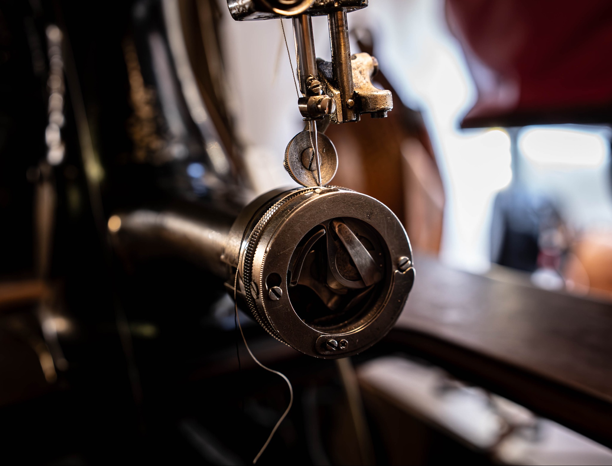 Detal z maszyny do szycia: igła, stopka i mechanizm chwytacza, oświetlone miękkim światłem. Widoczne ślady użytkowania i dbałości o sprzęt.