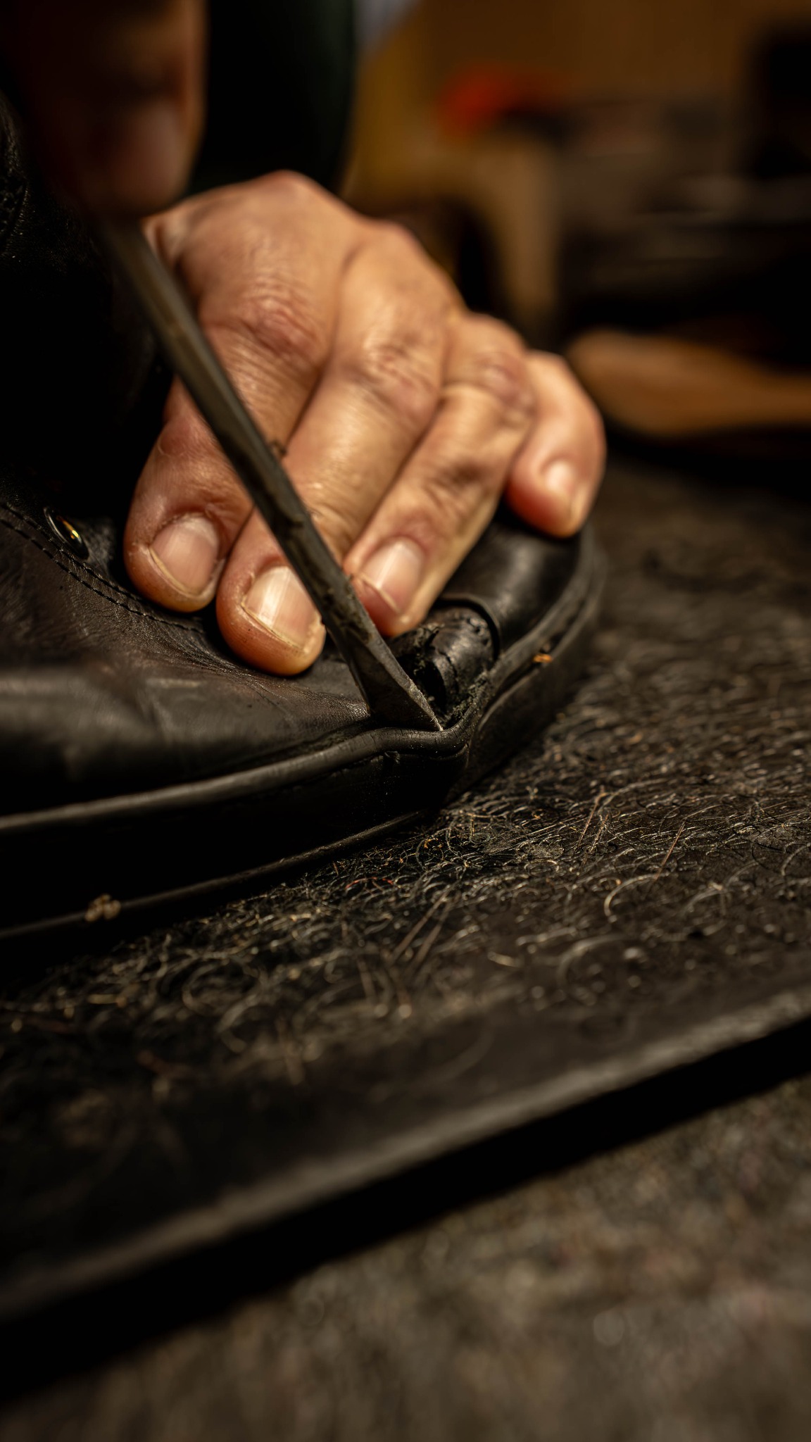Detail czarnego skórzanego buta, naprawianego ręcznie za pomocą szydła na warsztacie z widocznymi śladami pracy.