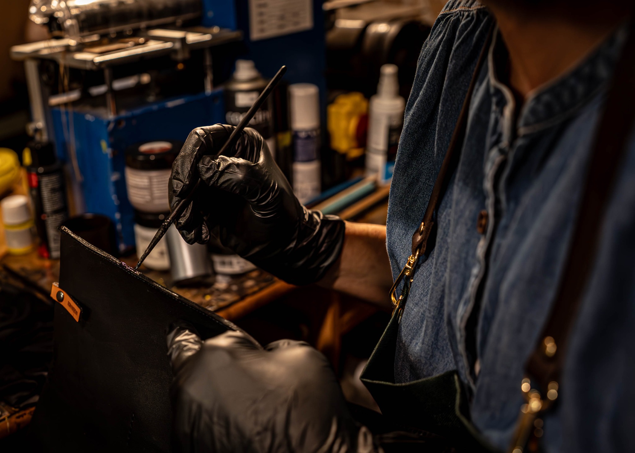 Ręczna praca kaletnicza w Bytomiu: osoba w rękawicach maluje krawędzie skórzanej torby pędzlem. Widoczne narzędzia i materiały kaletnicze.