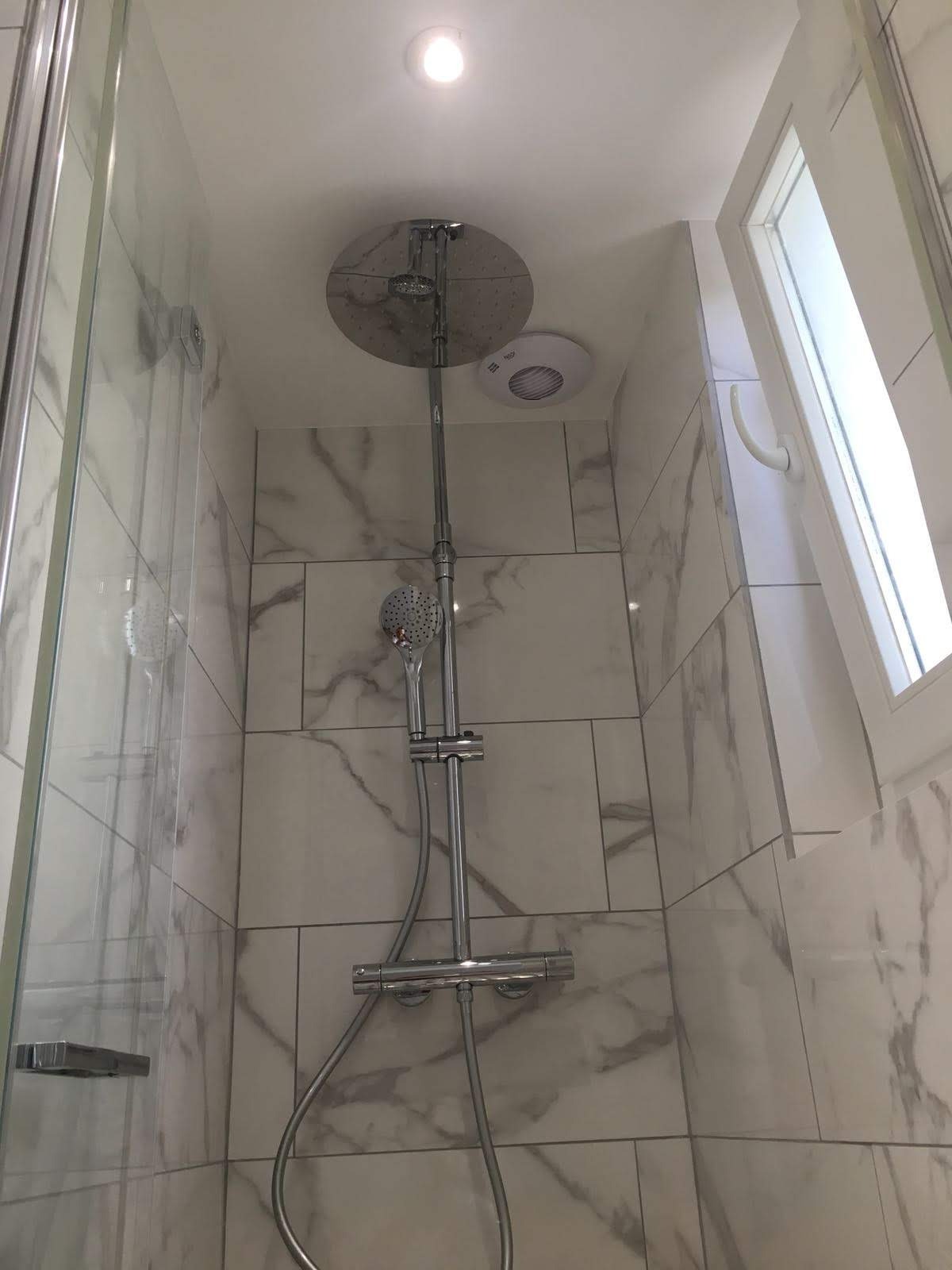 Nowoczesna kabina prysznicowa z marmurowymi płytkami. Deszczownica, słuchawka prysznicowa i termostat w chromowanym wykończeniu. Otwierane okno w tle.