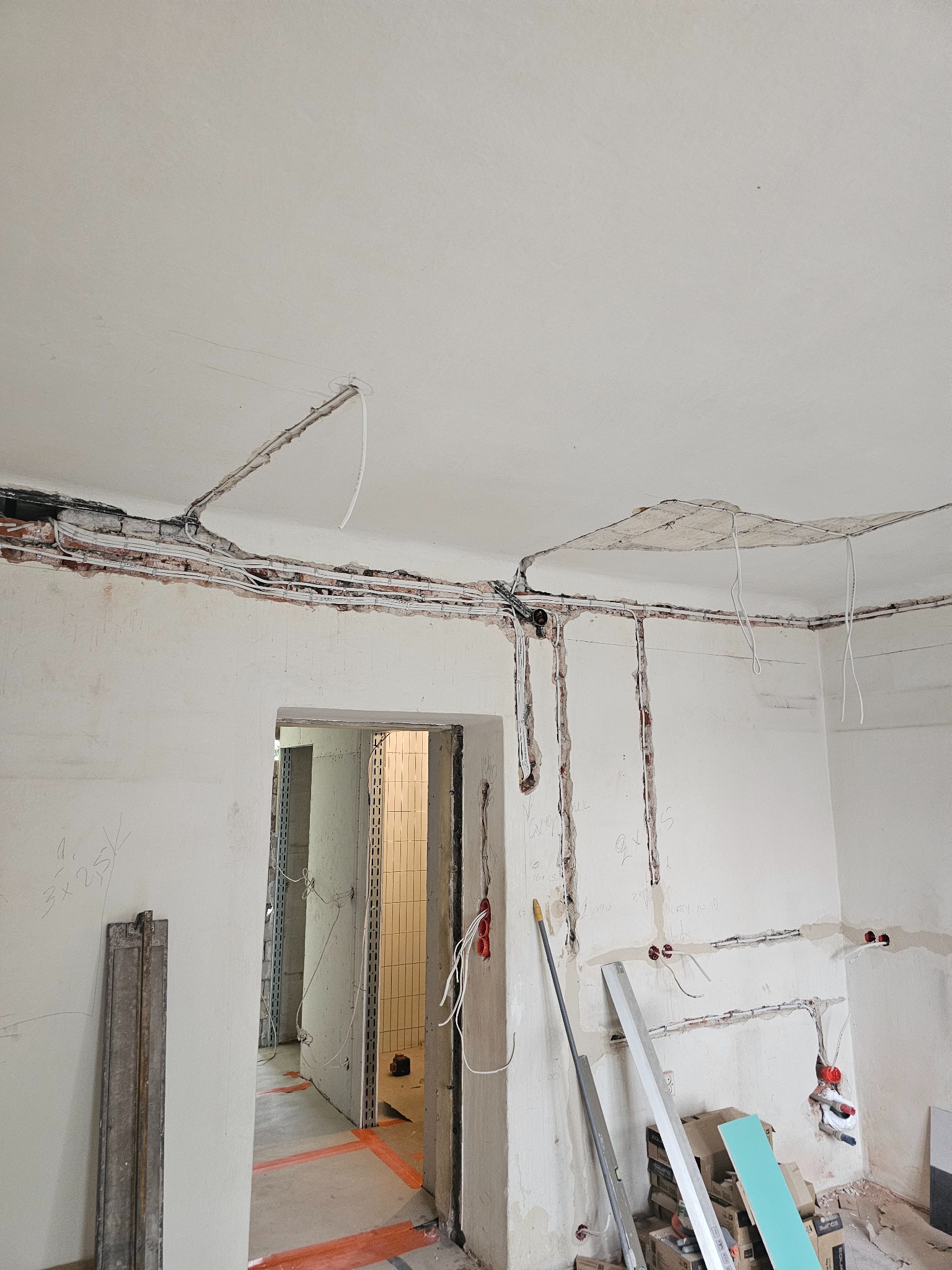 Wnętrze w trakcie remontu: odkryte przewody elektryczne w bruzdach na ścianach i suficie. Widoczne narzędzia i materiały budowlane. Stan surowy przed wykończeniem.