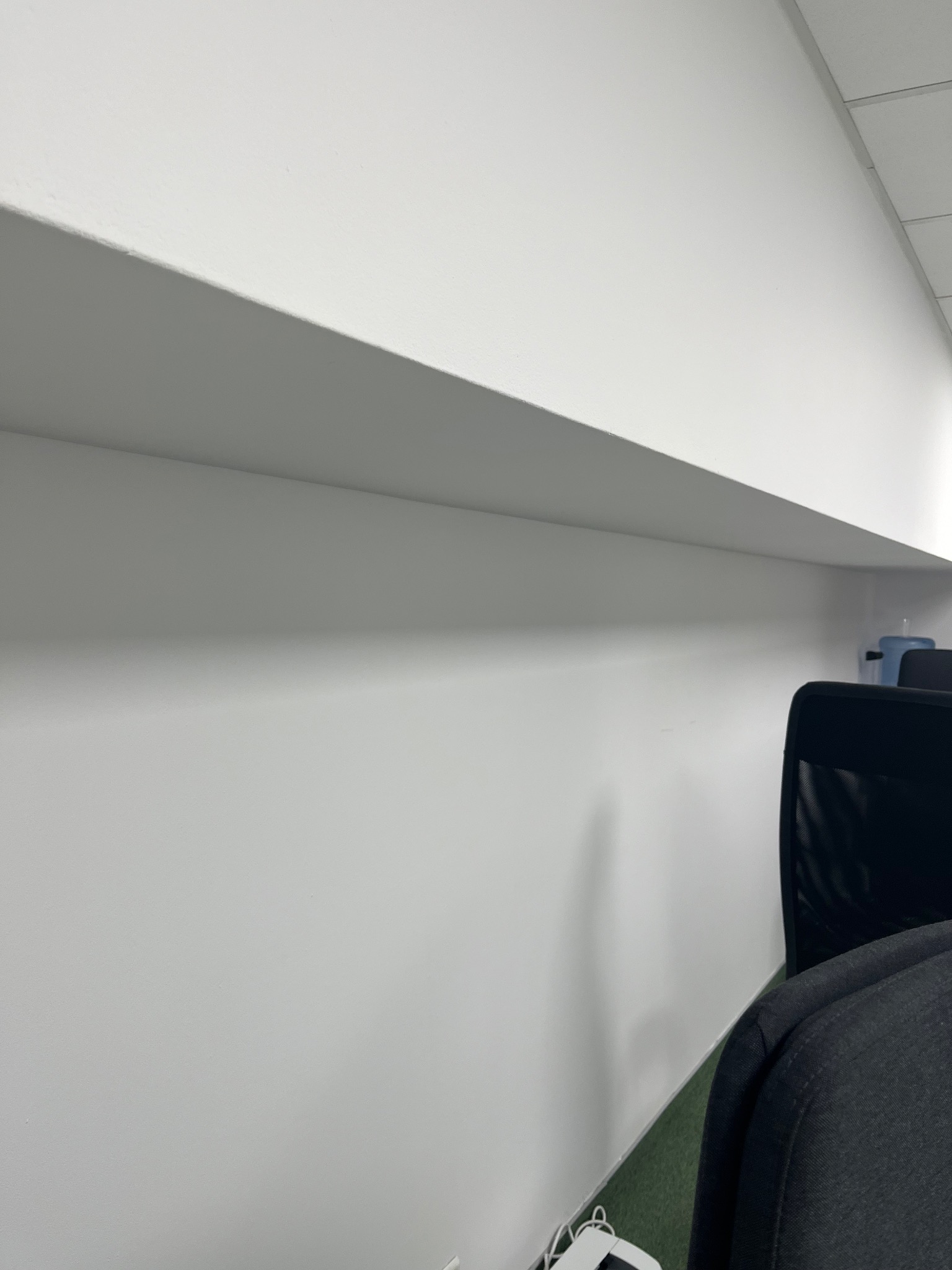 Świeżo pomalowana, gładka, biała ściana w biurze, widoczny fragment sufitu i krzesła biurowego. Minimalistyczne ujęcie, jasne oświetlenie.