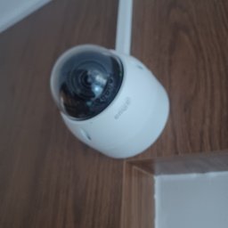 PROREM Rafał Kur - Kamera IP Dahua z anteną na tle drewnianej ściany i białego narożnika. Widoczny obiektyw kamery i logo producenta. Kamera skierowana w dół.